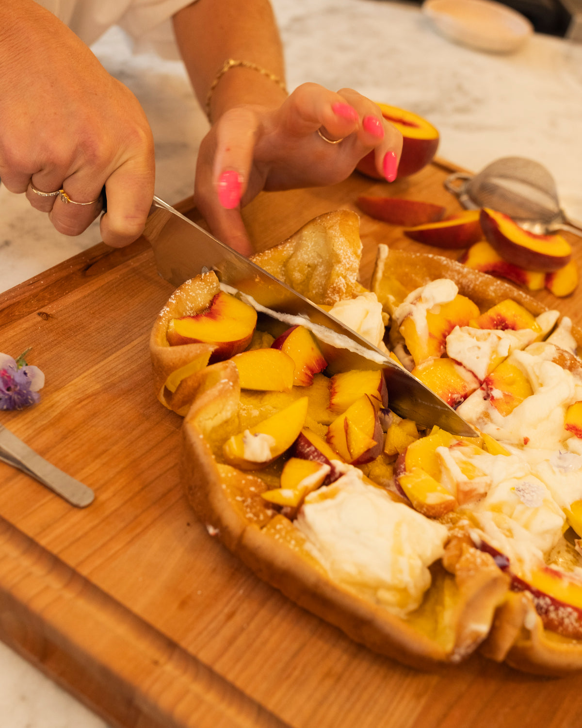 Hands slicing a baked peach dish on a wood butcher block