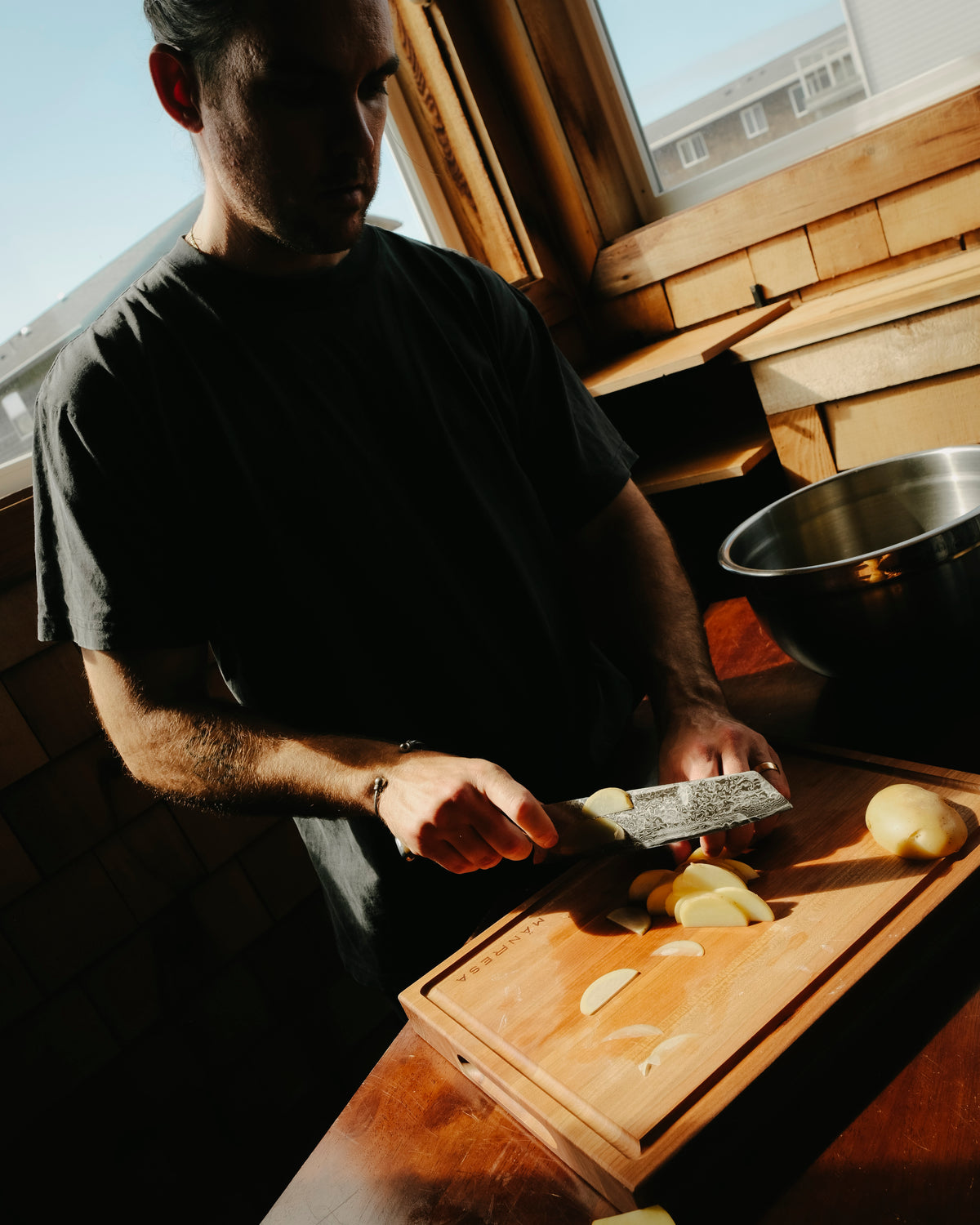 A cook slicing with a chef knife on a wood butcher block in a sunlit cabin kitchen