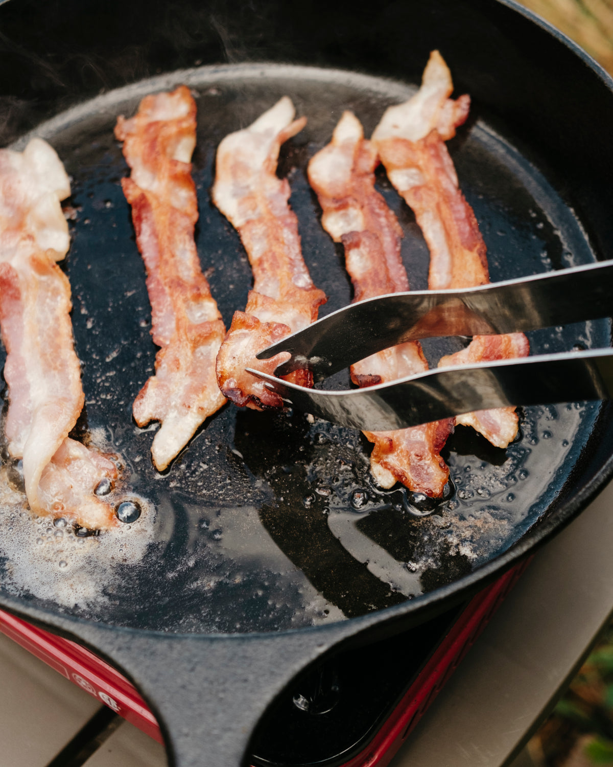 Bacon cooking in a cast-iron pan outdoors